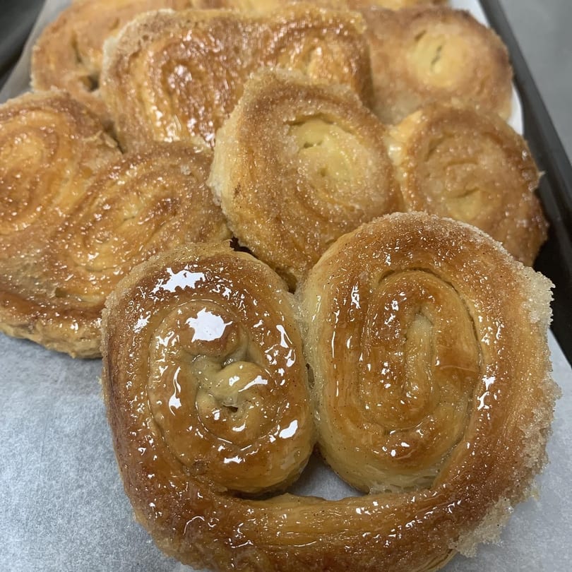 Close-up of golden-brown, sugar-glazed palmiers, some heart-shaped, on a white parchment-lined tray.