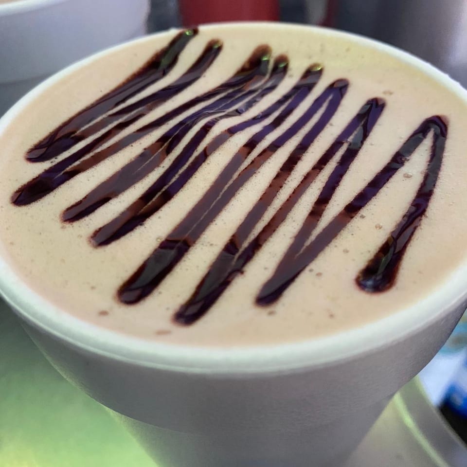 Close-up of a hot beverage in a white cup, topped with chocolate syrup drizzle.