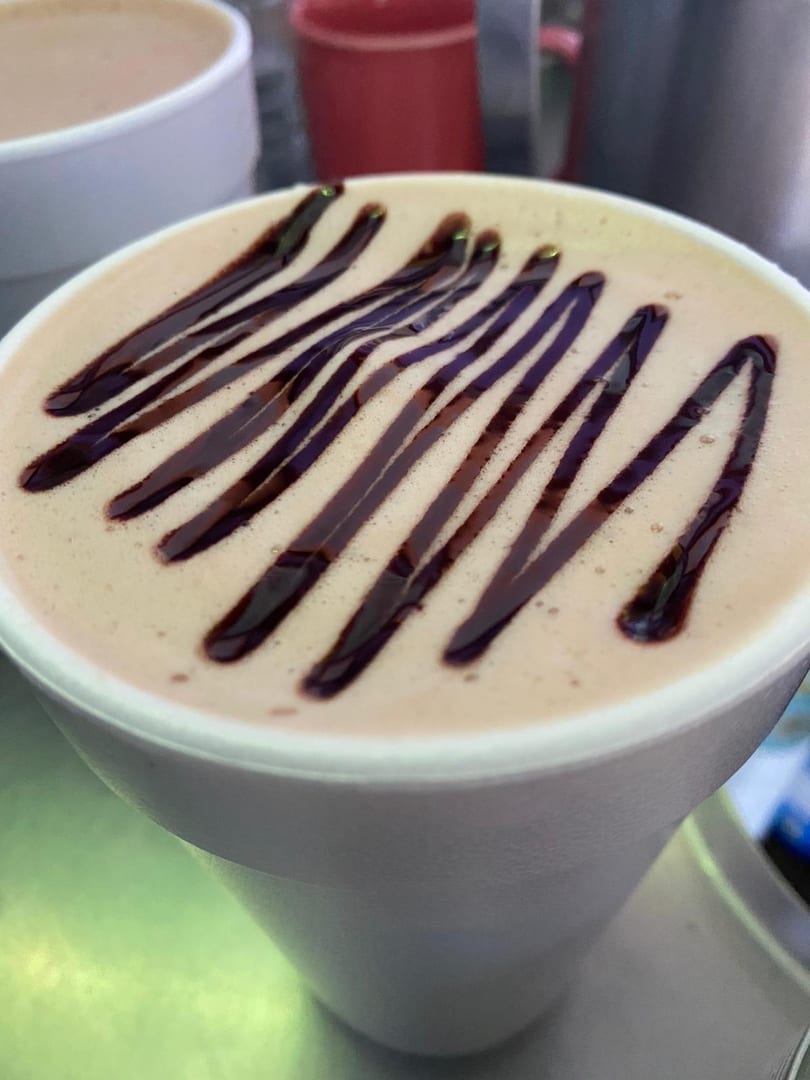 Close-up of a hot beverage in a white cup, topped with chocolate syrup drizzle.