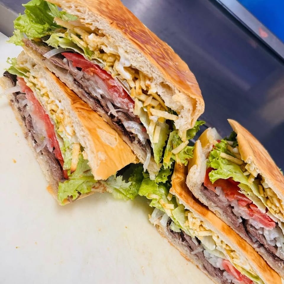 Two halves of a large sandwich filled with meat, lettuce, tomatoes, onions, and potato sticks.