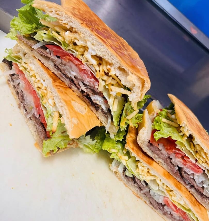 Two halves of a large sandwich filled with meat, lettuce, tomatoes, onions, and potato sticks.