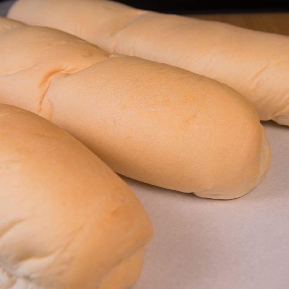 Three freshly baked, light golden brown bread loaves resting on parchment paper on a baking sheet.
