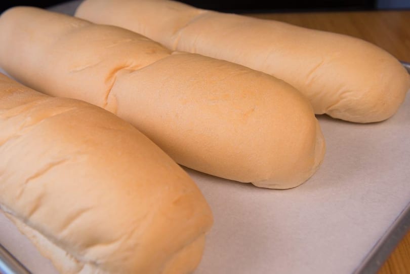 Three freshly baked, light golden brown bread loaves resting on parchment paper on a baking sheet.