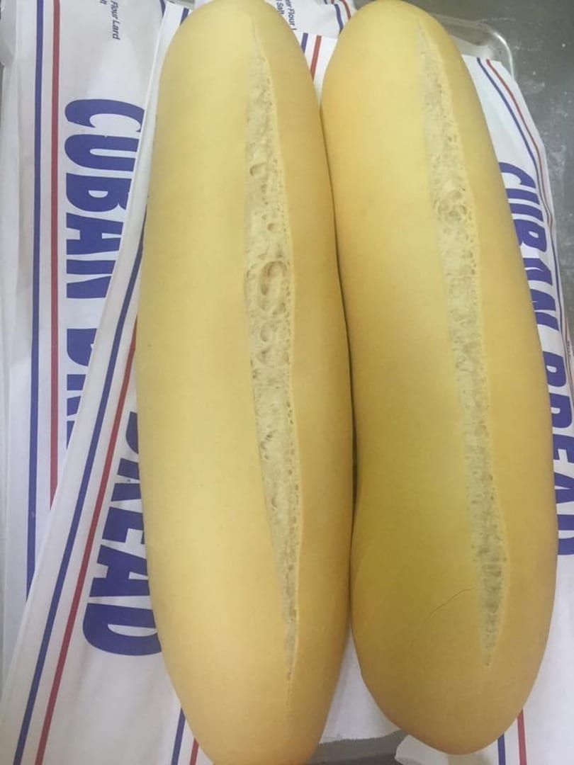 Two fresh Cuban bread loaves with a characteristic split down the middle, on a branded bag.