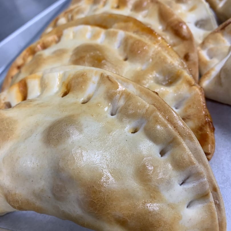 Close-up of several golden-brown baked empanadas with crimped edges on a white tray.