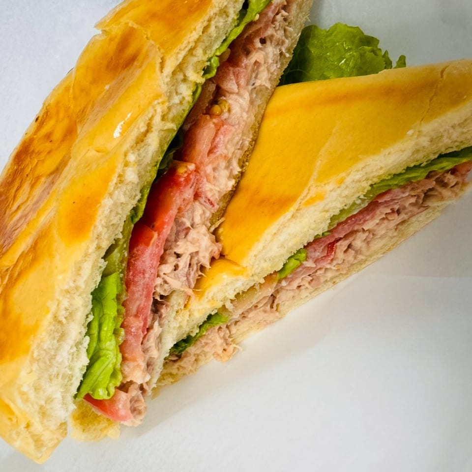 Two halves of a tuna sandwich with lettuce and tomato on a white background.