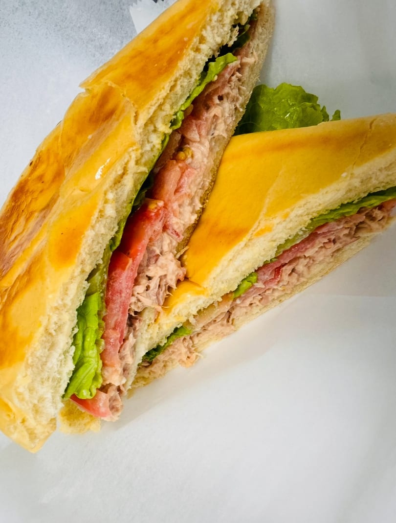 Two halves of a tuna sandwich with lettuce and tomato on a white background.