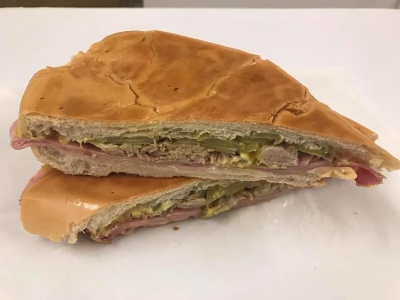 A Cuban sandwich, cut in half, revealing ham, pork, Swiss cheese, pickles, and mustard.