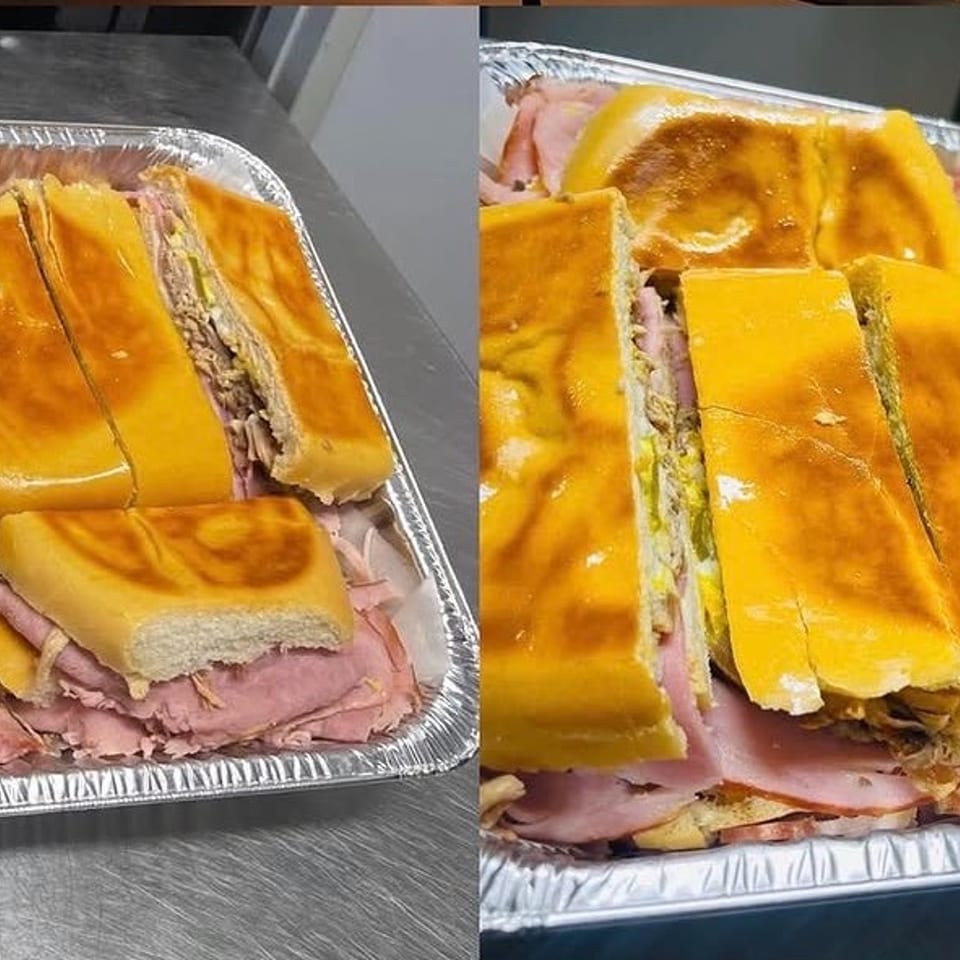 Two foil trays filled with sliced Cuban sandwiches, revealing ham, pork, cheese, and pickles.