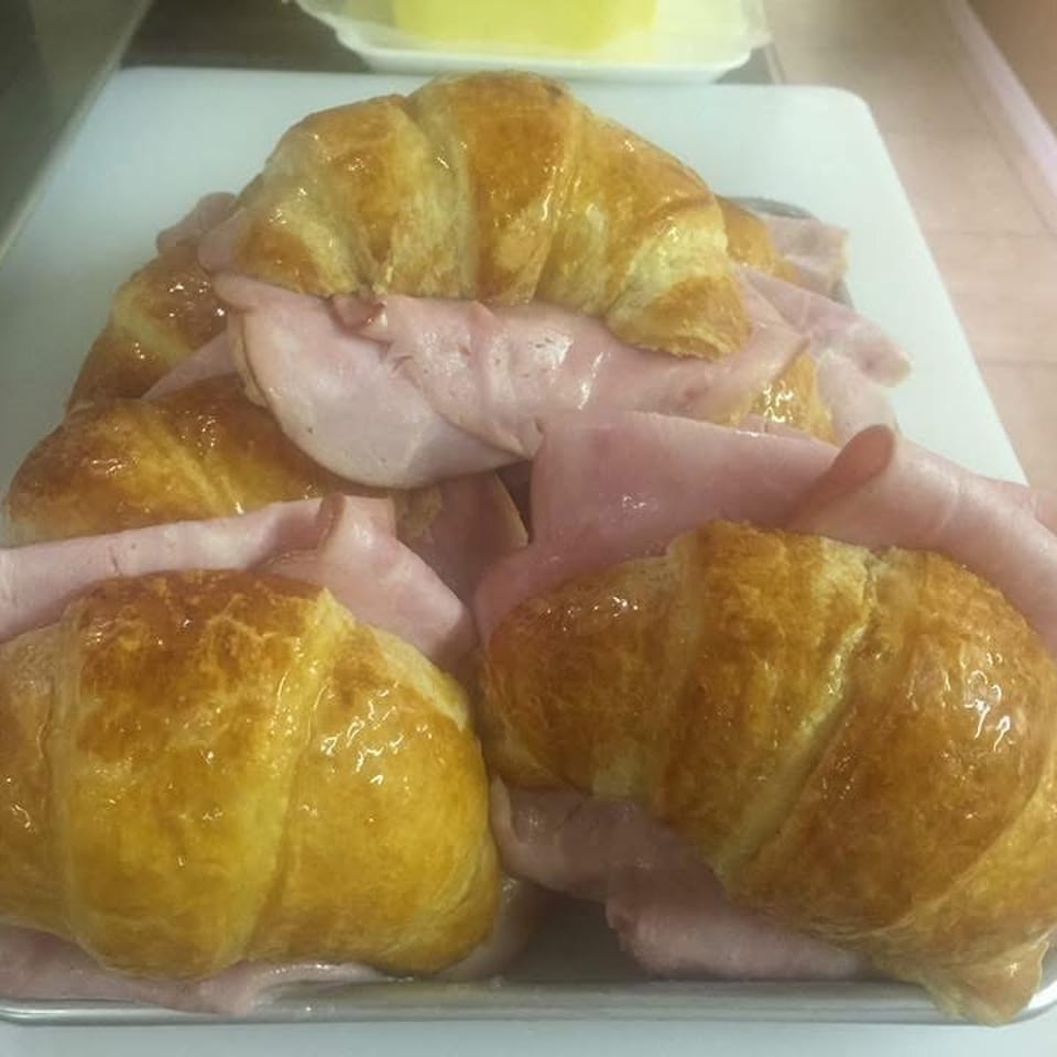Several golden croissants filled with thinly sliced pink ham on a white tray.