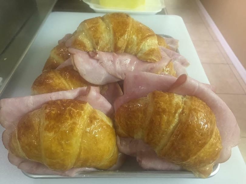 Several golden croissants filled with thinly sliced pink ham on a white tray.