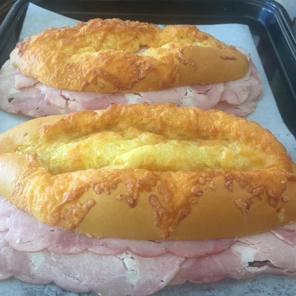 Two ham and cheese rolls on a baking sheet, ready to be cooked.