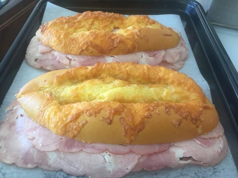 Two ham and cheese rolls on a baking sheet, ready to be cooked.