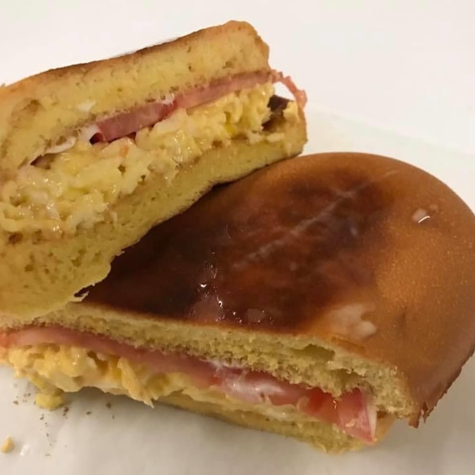 A toasted breakfast sandwich with scrambled eggs, ham, and tomato on a sweet bun.