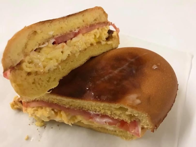 A toasted breakfast sandwich with scrambled eggs, ham, and tomato on a sweet bun.