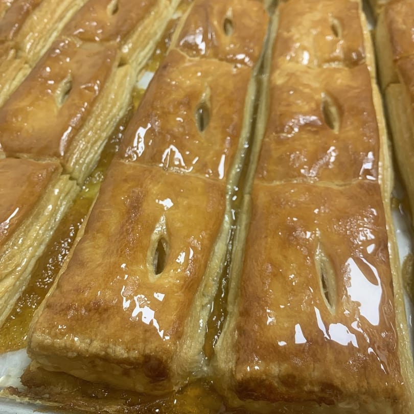 Rows of golden-brown, glazed pastries with small vents, glistening with syrup on a baking sheet.
