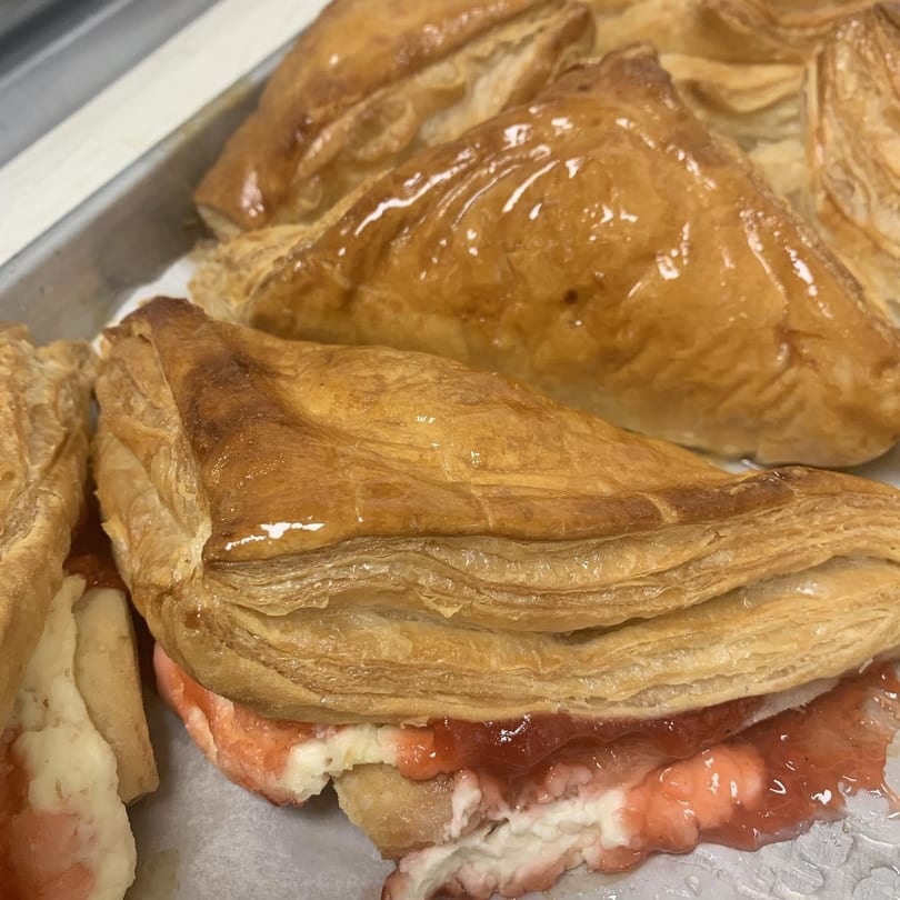 Golden brown puff pastry turnovers with strawberry and cream cheese filling on a baking sheet.