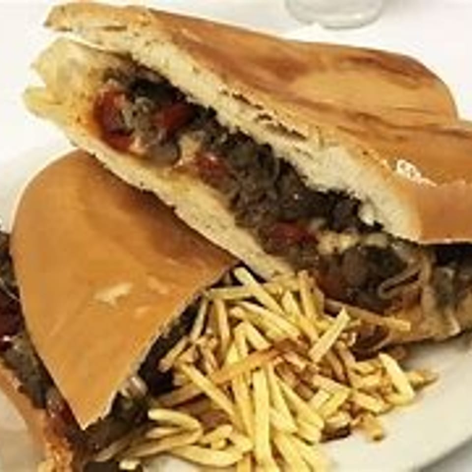 Two steak sandwiches with cheese, peppers, and onions, served with a side of shoestring fries.