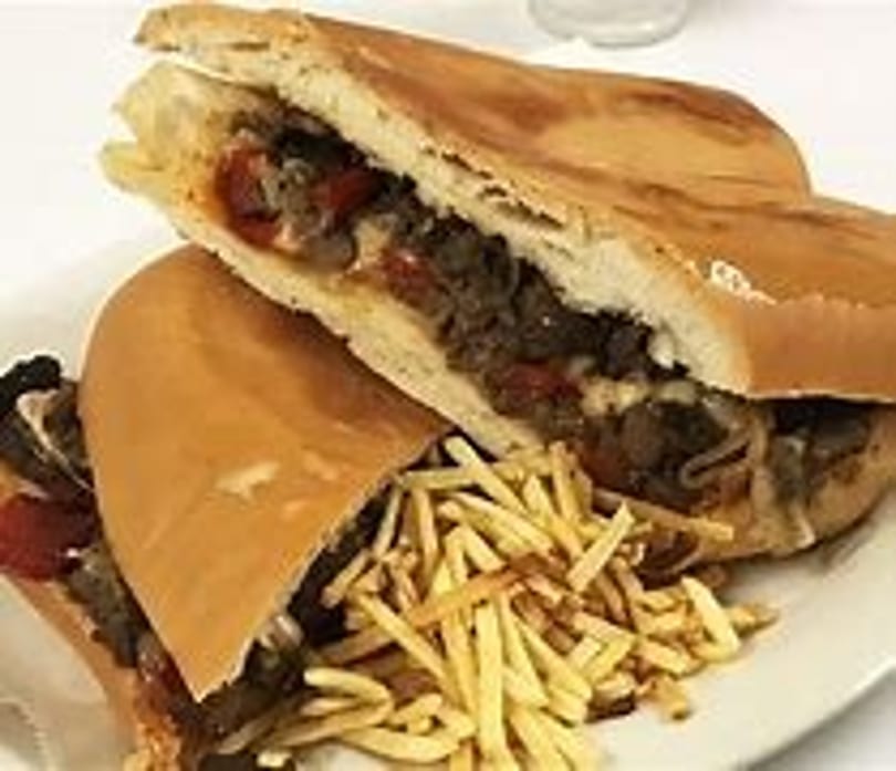 Two steak sandwiches with cheese, peppers, and onions, served with a side of shoestring fries.