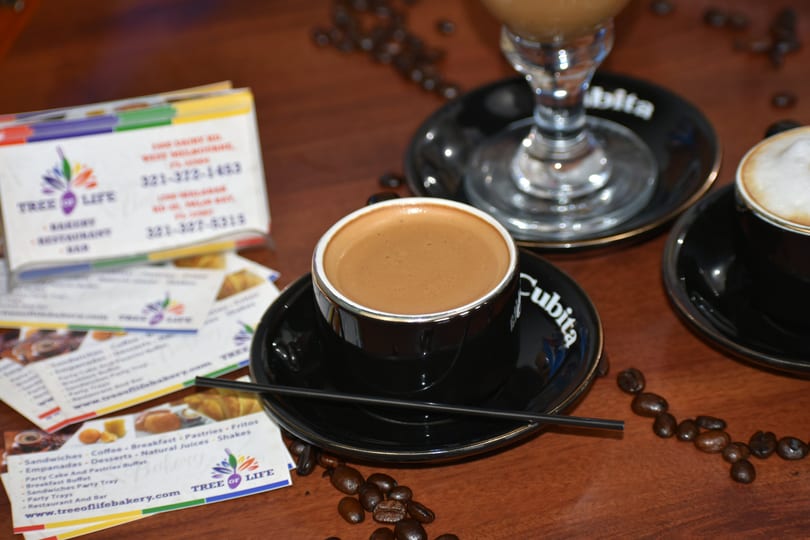 Three cups of coffee, two in black mugs and one in a tall glass, with coffee beans and business cards.