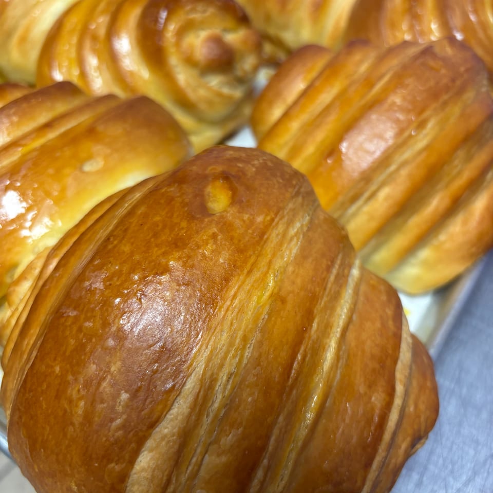 Close-up of several golden-brown, glazed croissants and pastries on a metal tray.