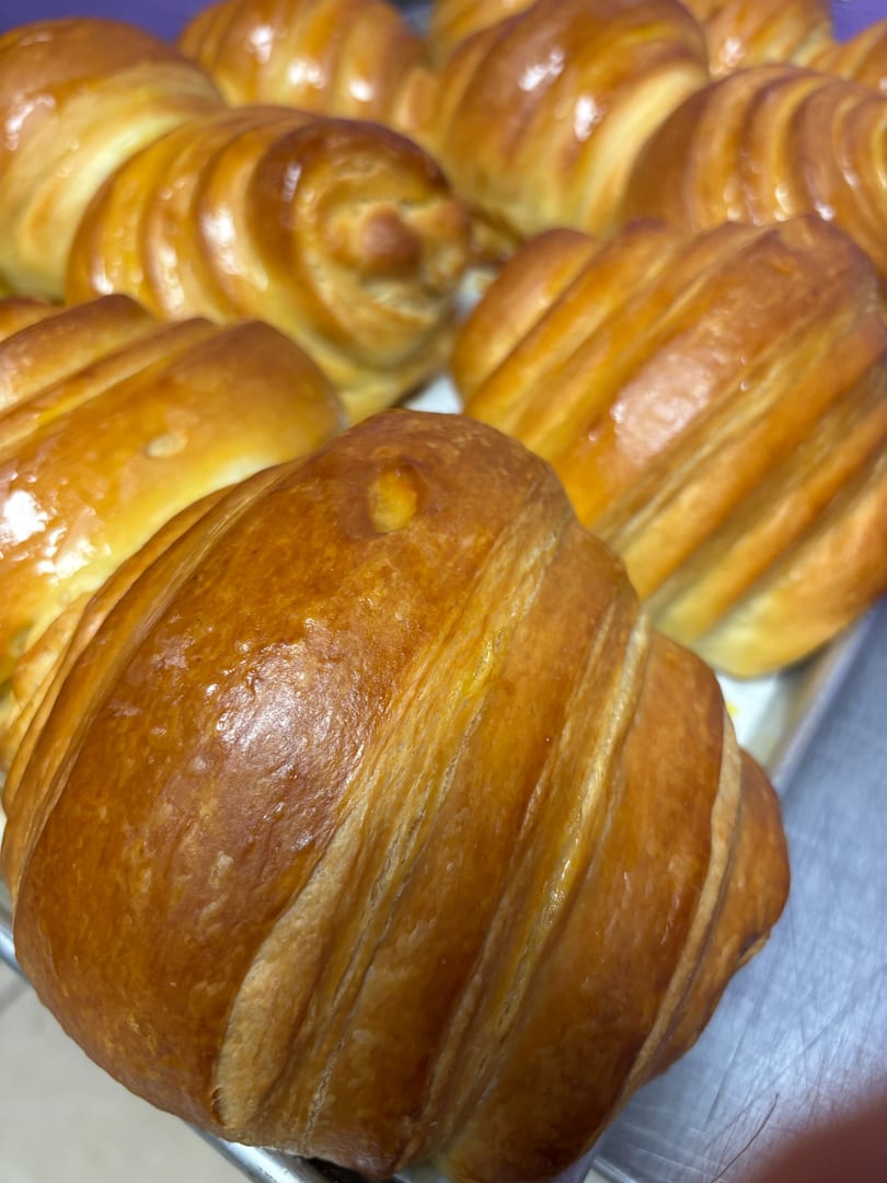 Close-up of several golden-brown, glazed croissants and pastries on a metal tray.