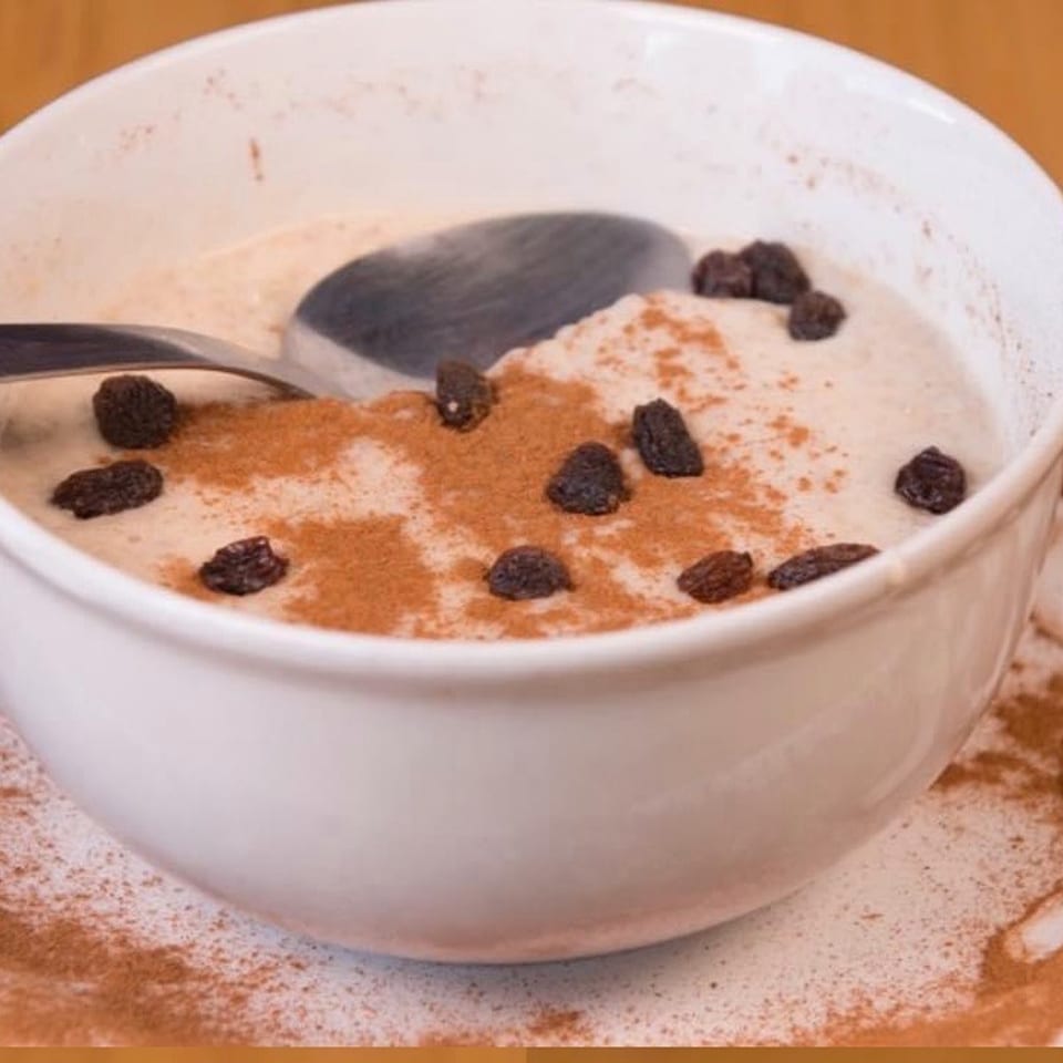 A white bowl of creamy oatmeal topped with cinnamon and raisins, with a spoon resting inside.
