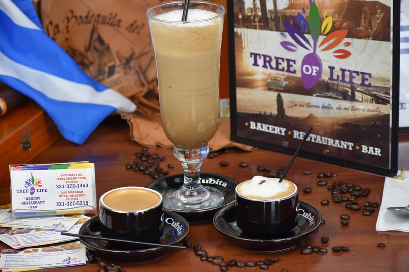 Three coffee drinks, business cards, and a Cuban flag on a wooden table.