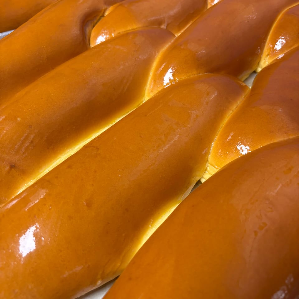 Rows of golden-brown braided challah bread loaves with a shiny glaze, fresh from the oven.