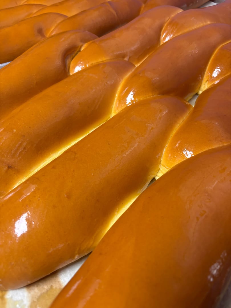 Rows of golden-brown braided challah bread loaves with a shiny glaze, fresh from the oven.