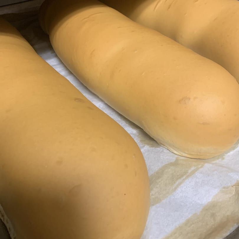 Three golden-brown, freshly baked bread loaves resting on a white parchment paper.