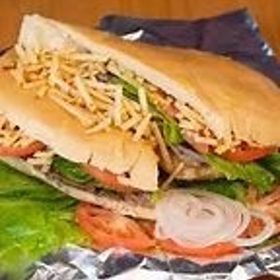 A large sandwich with lettuce, tomatoes, onions, and shoestring fries on foil.